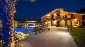 Une maison moderne à deux étages, dotée d’une piscine, d’un espace extérieur aménagé et d’un patio bien éclairé.