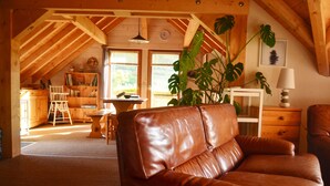 Un acogedor loft con sofá de cuero, vigas de madera, zona de comedor y un amplio ventanal con vistas.