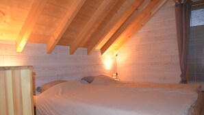 Un dormitorio con techo de madera, una cama con ropa blanca y una lámpara de pared.