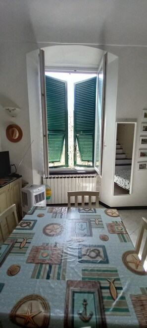Una habitación con un ventanal grande, un radiador, una mesa con mantel de motivos náuticos y una cama con colcha estampada.