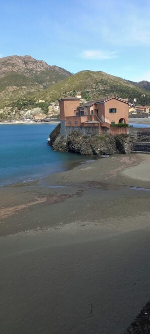 A coastal building with a stone foundation, adjacent to a beach and a rocky shoreline.