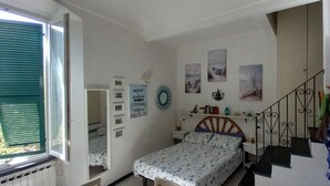Ein Schlafzimmer mit Bett, Nachttisch, Kommode, Fenster mit Jalousien, einer Bilderwand und einer Treppe.