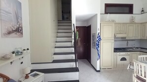 Eine Küche mit weißen Schränken, einem Esstisch und einer Treppe, die in einen anderen Raum führt.