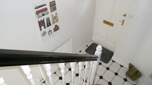 Una escalera con balaustres blancos, una puerta blanca con un ventanal y un cartel con diversas ilustraciones de edificios en la pared.