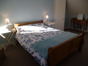 Un dormitorio con una cama de madera, dos mesitas de noche con lámparas, un escritorio con silla y una puerta.