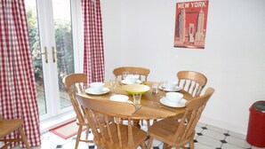 Un comedor con una mesa redonda de madera dispuesta para cuatro personas, rodeada de sillas de madera. En la pared hay un cartel que muestra el Empire State Building.