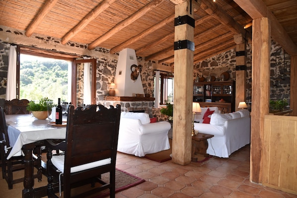 A rustic interior with stone walls, wooden beams, a fireplace, white upholstered furniture, and a dining table with chairs. - DREAM LOCATION in SARDINIA: stunning private hunting lodge minutes from beach (Orosei)