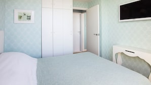 Une chambre à coucher comprenant un lit, une armoire, un téléviseur et une porte donnant sur une autre pièce.