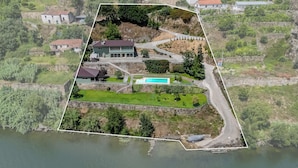 An aerial view of a property with a swimming pool, a large house, and a surrounding landscape.