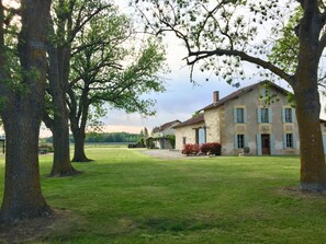 Un grand bâtiment en pierre, doté d’un toit en pente, entouré d’une pelouse bien entretenue et de plusieurs grands arbres.