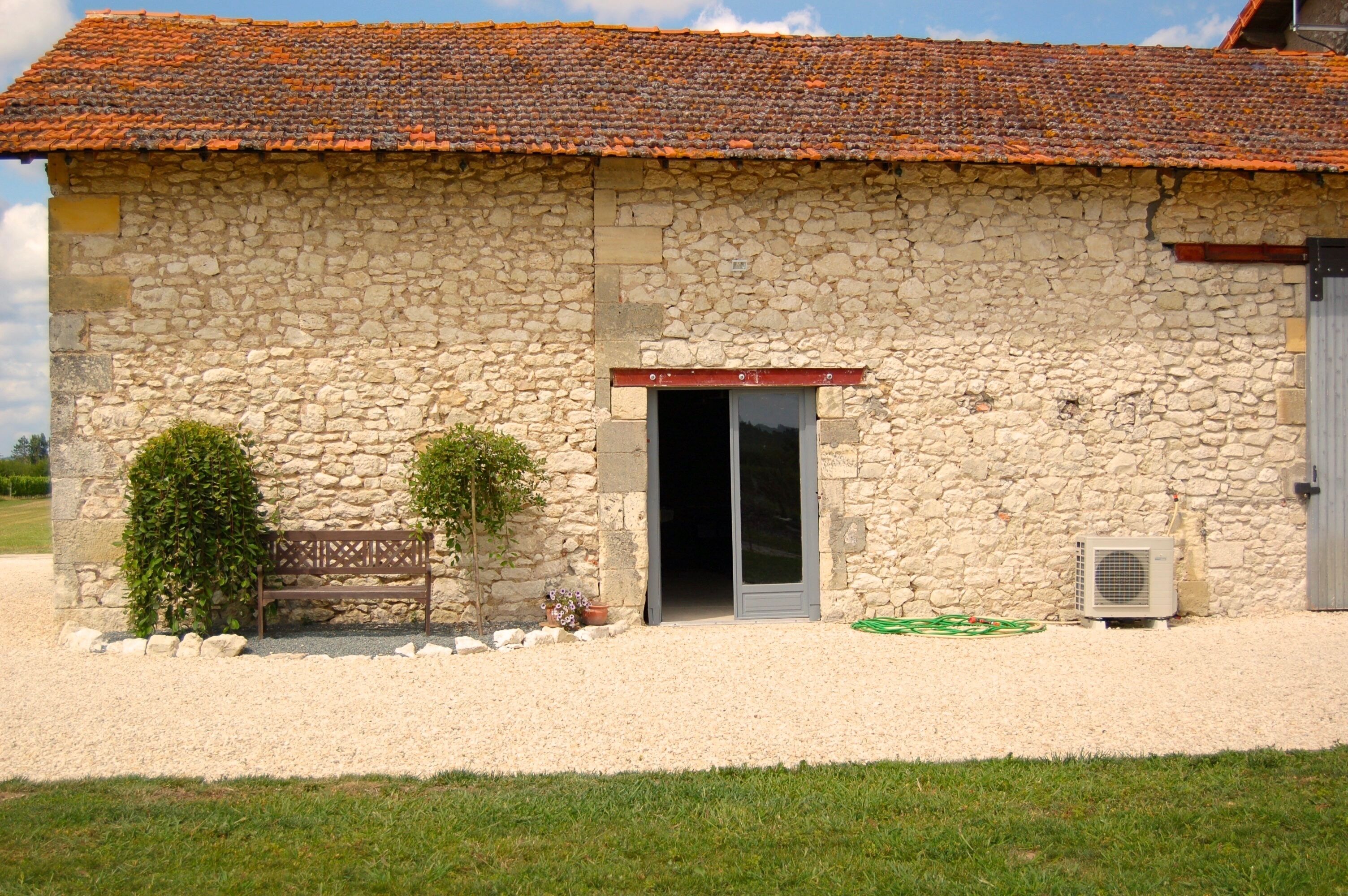 A stone building with a tiled roof, a wooden bench, and a door.