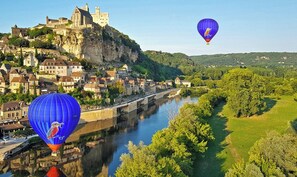 Eine historische Stadt mit einem Schloss auf einem Hügel, einem Fluss und Heißluftballons.