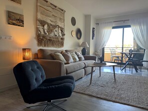 A living room with a sofa, a black chair, a coffee table, and a dining area with chairs and a table.