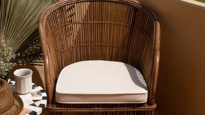 Una silla de mimbre con cojín en un balcón con vista a un campo de golf y colinas.