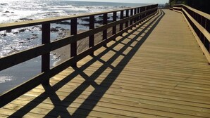 Un muelle de madera que lleva a la playa, con barandilla en un lado.