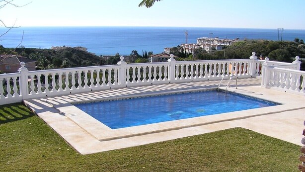 A rectangular swimming pool with a white balustrade, surrounded by a well-maintained lawn, and overlooking a coastal landscape with buildings in the distance. - BENALMADENA Villa Apartment,close to beach, nice private pool Internet/Wifi (Benalmádena)
