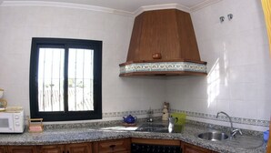 A kitchen with a window, wooden cabinets, a stove, and a sink. - BENALMADENA Villa Apartment,close to beach, nice private pool Internet/Wifi (Benalmádena)