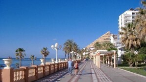 A coastal promenade with a paved walkway, palm trees, and a building with balconies overlooking the sea. - BENALMADENA Villa Apartment,close to beach, nice private pool Internet/Wifi (Benalmádena)