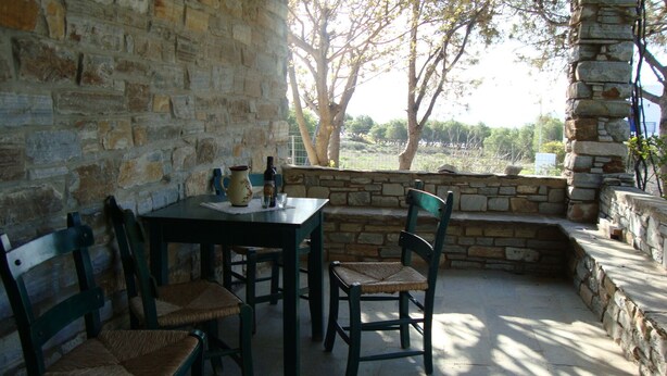 A stone-walled outdoor seating area with a table and chairs, overlooking a garden. - Perfect for a for a quiet relaxing vacation, very close to 2 of the best beaches (Tinos)