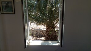 A room with a bed, a window with a view of a palm tree and a stone wall outside. - Perfect for a for a quiet relaxing vacation, very close to 2 of the best beaches (Tinos)