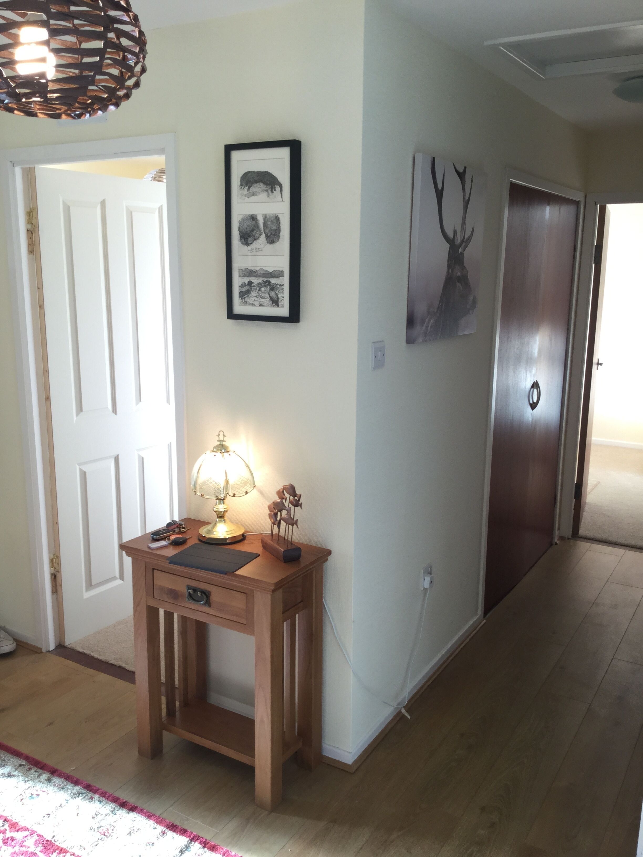 A hallway with a wooden desk, a lamp, and framed artwork on the wall.