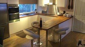 A modern kitchen with a wooden countertop, stainless steel appliances, and a bar area with stools. - A loch side property with stunning views located in a walker's paradise. (Inverinate)