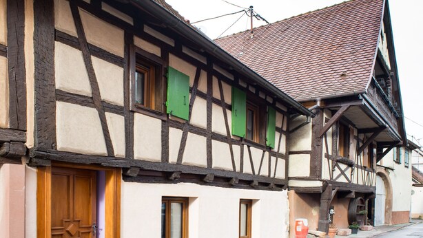 Un edificio tradicional con entramado de madera, una puerta de madera, varias ventanas y un tejado de tejas rojas.
