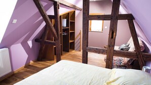 Un dormitorio con techo inclinado, vigas de madera, cama, armario y un escritorio pequeño con silla.