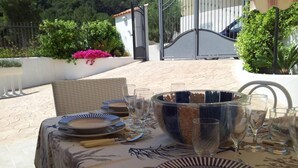 Un área de comedor al aire libre con una mesa dispuesta para cuatro, rodeada de sillas y un cuenco grande de frutas.