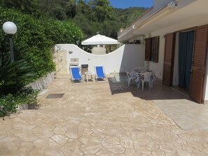 Un espace patio avec un sol en pierre, deux fauteuils bleus, une petite table et un parasol blanc.