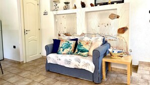 Una habitación con un sofá estampado en cuadros, una pequeña mesa de madera y una estantería con adornos.
