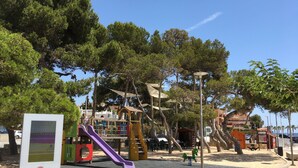 Un parque infantil con toboganes y estructuras para escalar, rodeado de árboles y un cielo despejado.
