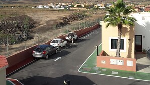 A parking area with cars, a building with a palm tree, and a mountain in the background. - 60sq.m Roof Solarium, 50sq.m Rear Terrace: BBQ, Fibre WiFi, TV (BBC, SKY sports) (Corralejo)