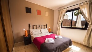 A bedroom with a bed, nightstands, a window with curtains, and a view of the outside. - 60sq.m Roof Solarium, 50sq.m Rear Terrace: BBQ, Fibre WiFi, TV (BBC, SKY sports) (Corralejo)