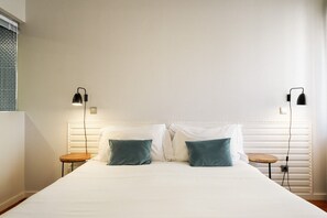 A neatly made bed with two pillows, two bedside tables, and two wall-mounted lamps.