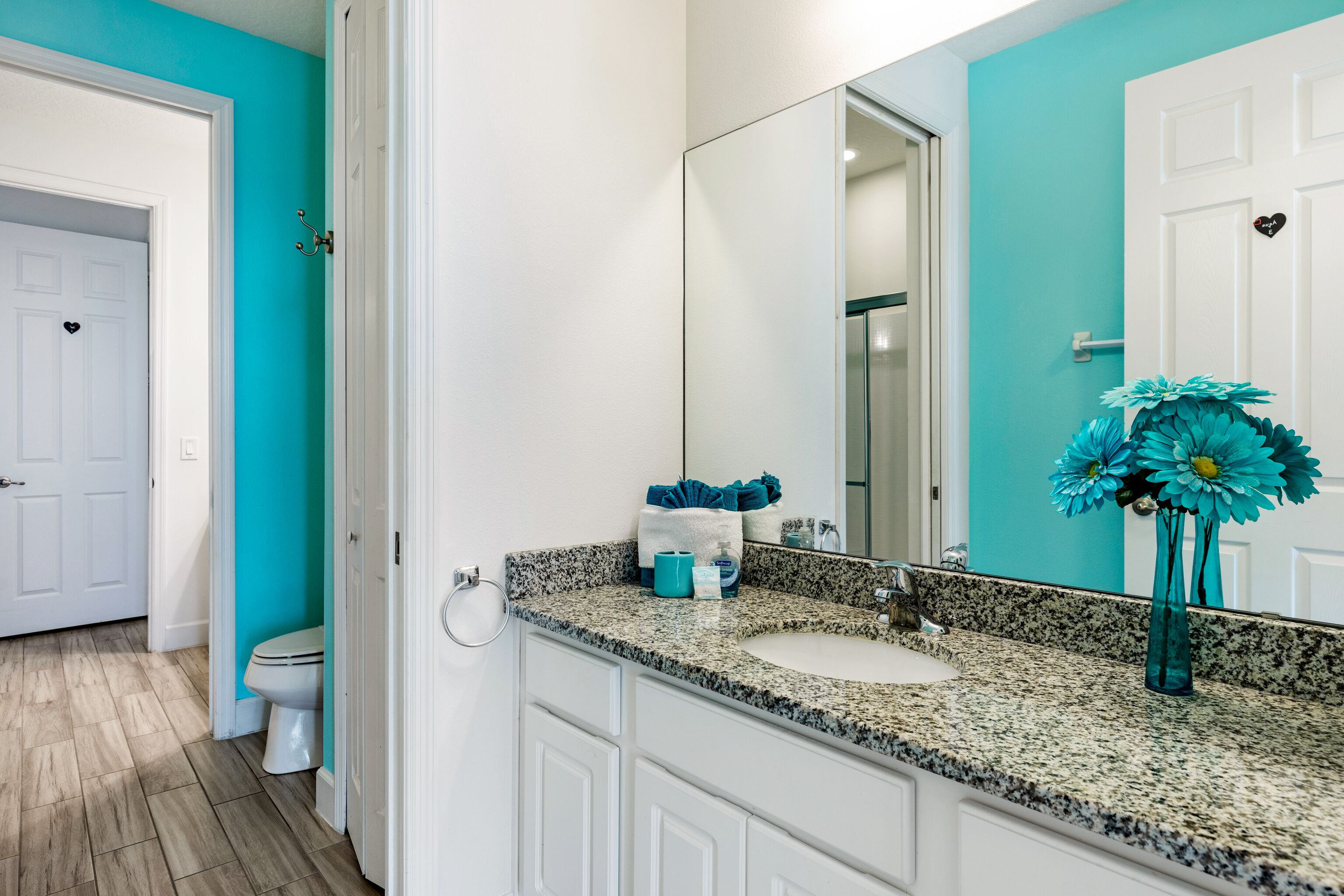 A bathroom with a granite countertop, white cabinets, a sink, a mirror, and a toilet.