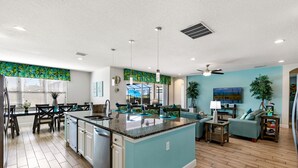 A modern kitchen with a central island, a dining area with dark chairs, and a living room with a sofa and a coffee table. - South View Luxury 5★ Villa: Pool, Spa, Game Room, Near Disney & Universal (Davenport)