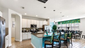 A modern kitchen with white cabinets, a granite countertop, and a central island with bar stools. - South View Luxury 5★ Villa: Pool, Spa, Game Room, Near Disney & Universal (Davenport)