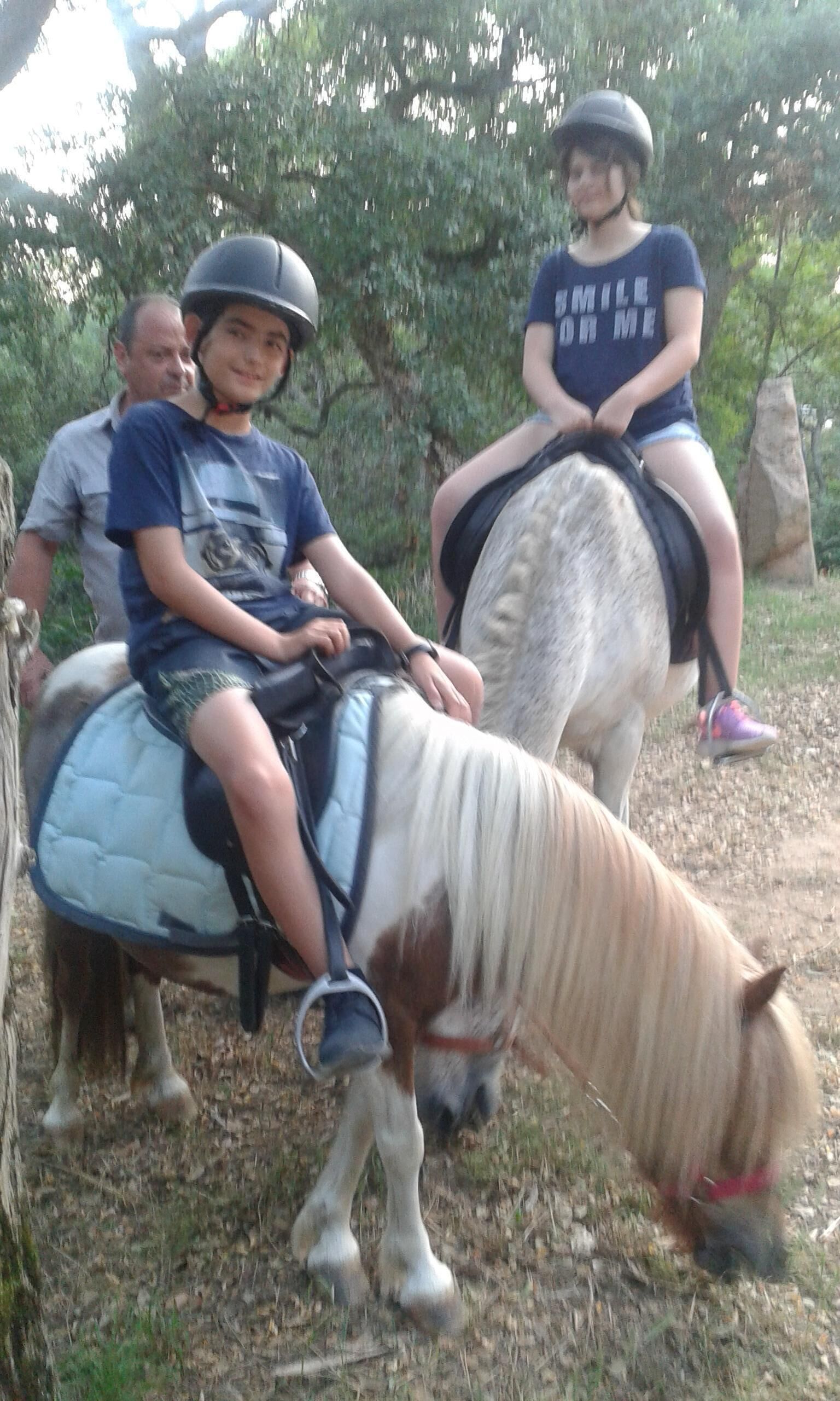 Three people riding a small white horse with a blue saddle.