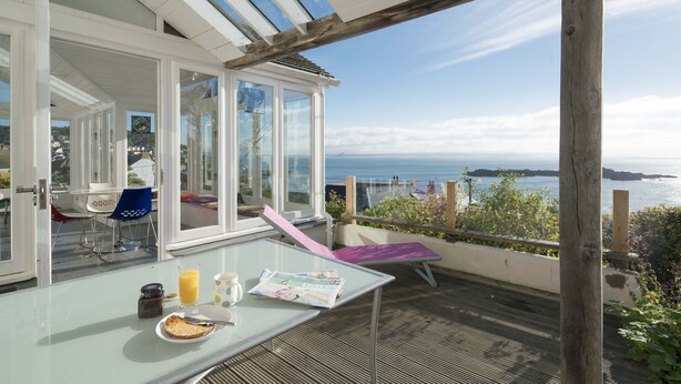 A balcony with a table, chairs, and a glass door leading to a room. - Light filled home from home with spectacular panoramic sea views of Mounts Bay (Mousehole)