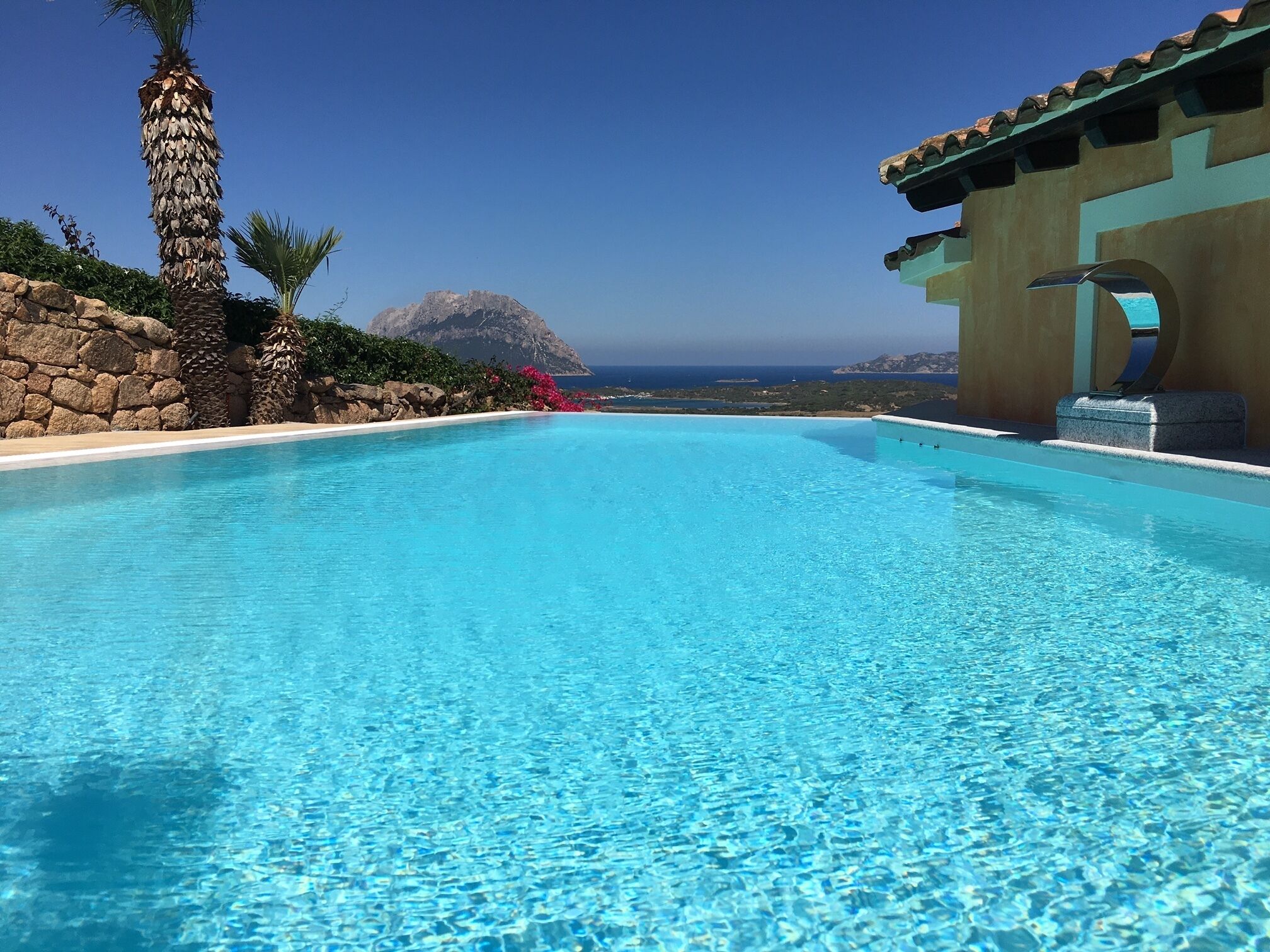 A clear blue infinity pool with a view of the ocean and a mountain in the background.