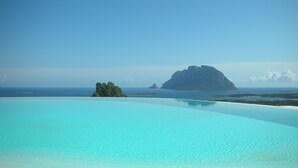 A clear blue infinity pool with a view of a distant island and the ocean.