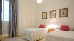 A room with two single beds, a wooden nightstand with a lamp, a wardrobe, and a window with curtains. - Beautiful apartment in  historical recently reformed building. (Sevilla)