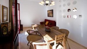 A dining area with a wooden table and wicker chairs, a red sofa, and a chandelier. - Beautiful apartment in  historical recently reformed building. (Sevilla)