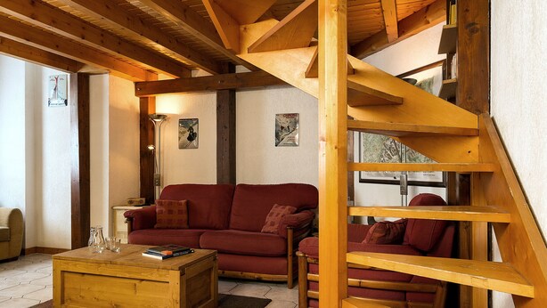 Ein großzügiger Wohnbereich mit einer Holztreppe, einem roten Sofa und einem Couchtisch aus Holz.
