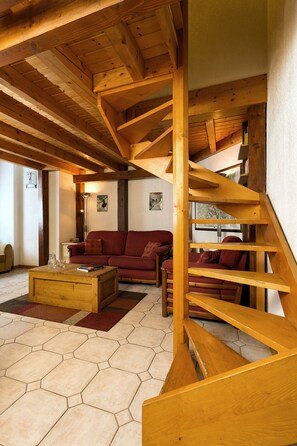 Amplia sala de estar con una escalera de madera, un sofá rojo y una mesa de centro de madera.