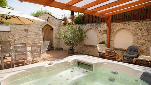 Un jacuzzi con pared de piedra de fondo, asientos exteriores y una pérgola de madera.