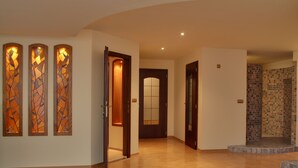 Un pasillo amplio con suelo de madera, zona de ducha con azulejos y una puerta que da a otra habitación.
