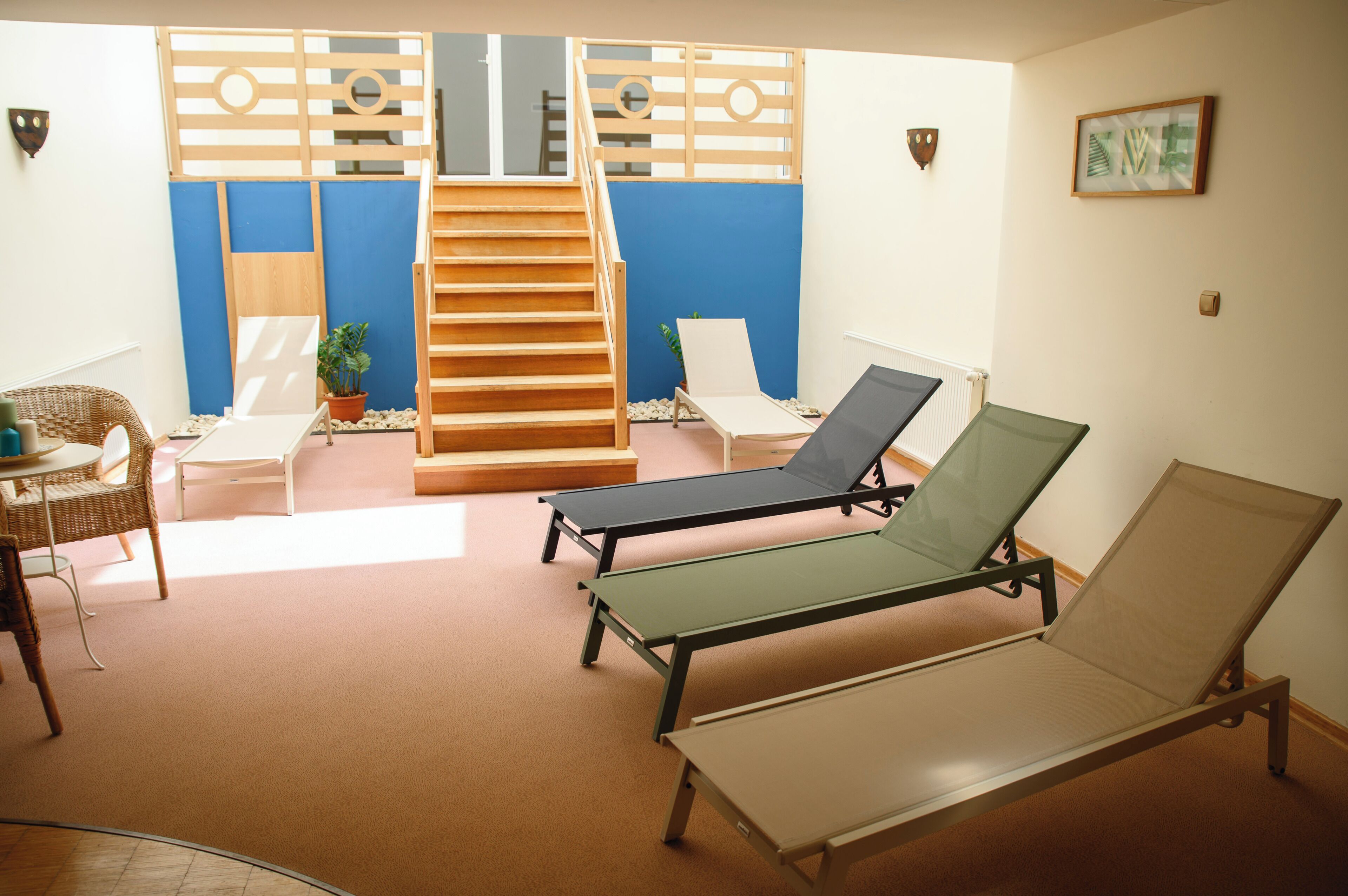 A room with a staircase, lounge chairs, a wicker chair, and a small table.