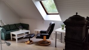 Una stanza in stile loft con soffitto spiovente, un divano verde, una poltrona nera, un tavolo bianco e una stufa a legna.
